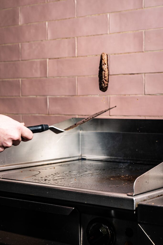 Patty wordt omgedraaid op de hete plaat in de keuken van Diego's
